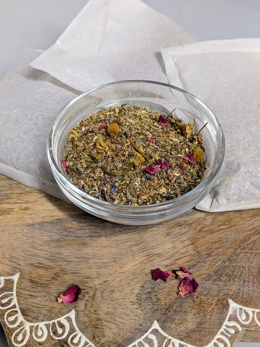 Herbal tea mix in a glass bowl on a wooden surface with a white cloth.