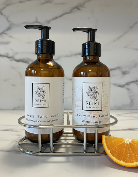 Two bottles of Reimi Naturals hand soap and lotion on a stand with light gray background