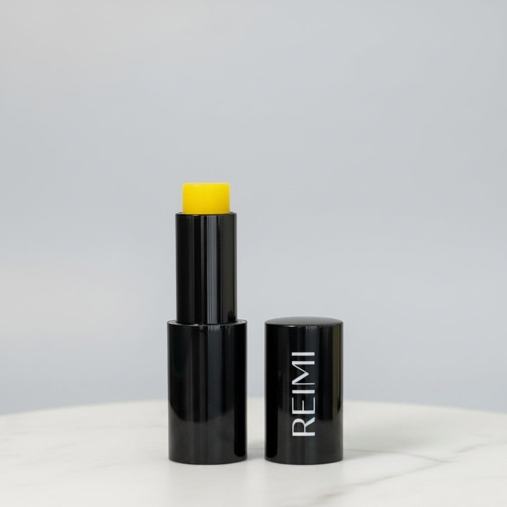 Black Lip stick container with yellow lip balm on a gray background