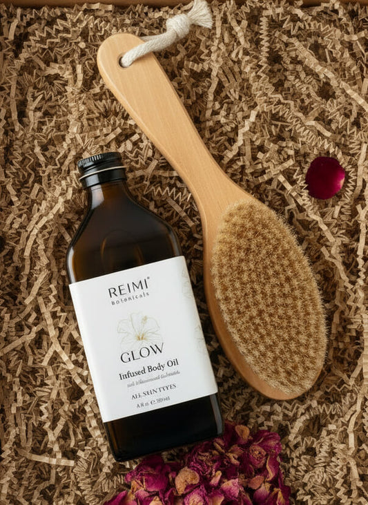 Bottle of Reimi Glow Infused Body Oil with a wooden brush on a textured surface.