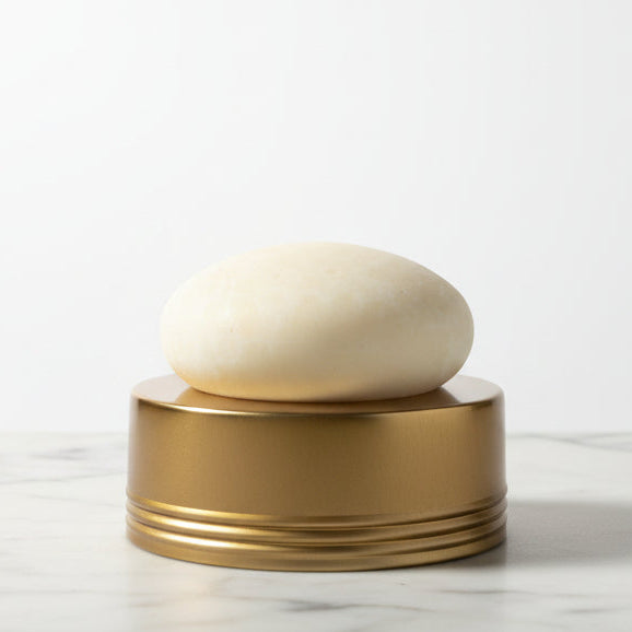 Round white lotion bar on a gold cylindrical container on a white marble countertop