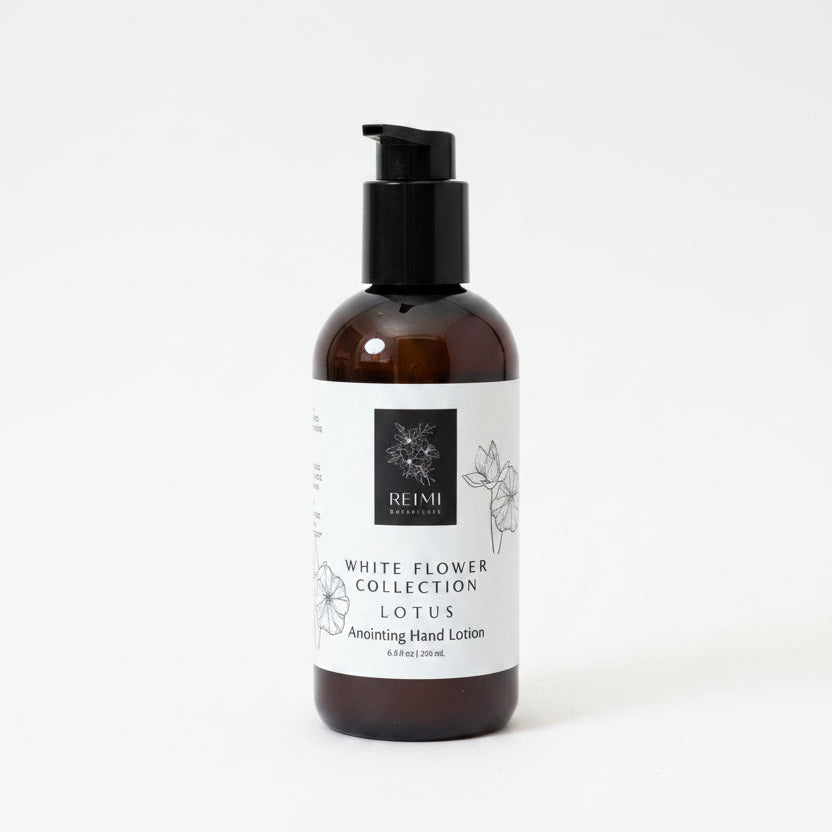 A bottle of REIMI White Flower Collection Lotus Soothing Hand Lotion standing on a textured beige mat against a brown cardboard background.