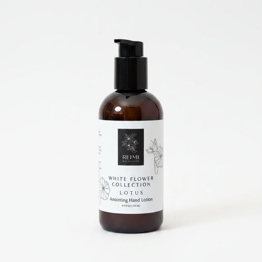 A bottle of REIMI White Flower Collection Lotus Soothing Hand Lotion standing on a textured beige mat against a brown cardboard background.