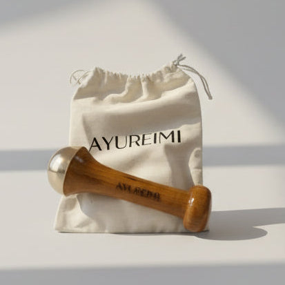 Wooden tool with gold head on a white drawstring bag with 'AYUREIM' branding.