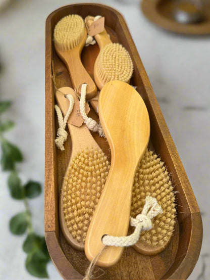 Set of wooden brushes in a wooden tray on a table with a pink towel and bottles in the background.